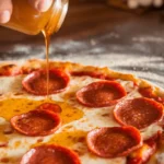 Close-up of hot honey being drizzled over a freshly baked pizza topped with crispy pepperoni and melted mozzarella cheese, highlighting the golden honey's shine