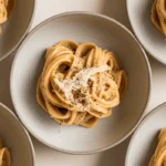 Multiple bowls of Cacio e Pepe pasta, each featuring a swirl of creamy noodles garnished with cheese and pepper.