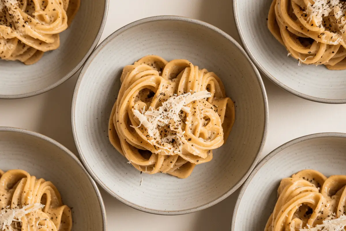 Multiple bowls of Cacio e Pepe pasta, each featuring a swirl of creamy noodles garnished with cheese and pepper.